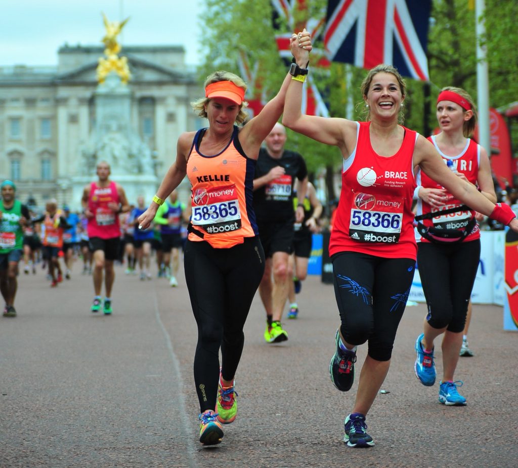 Two women holding hands and running towards the end of the London Marathon