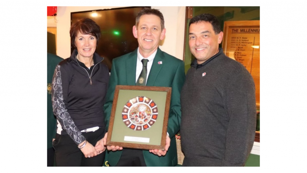 Three people stood looking at the camera. The middle person is holding a golfing plaque.