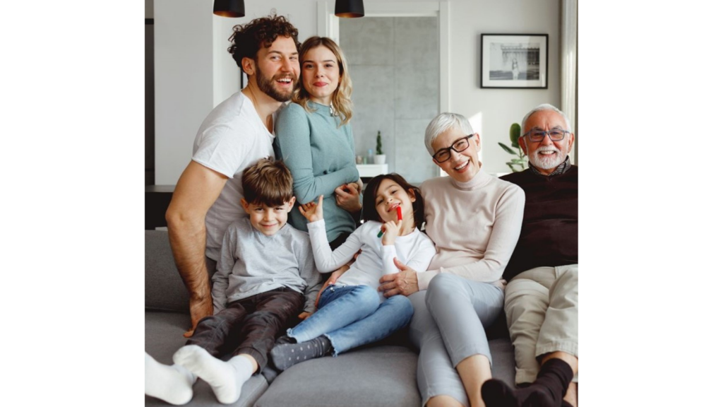 A young family with grandparents sat on a sofa.
