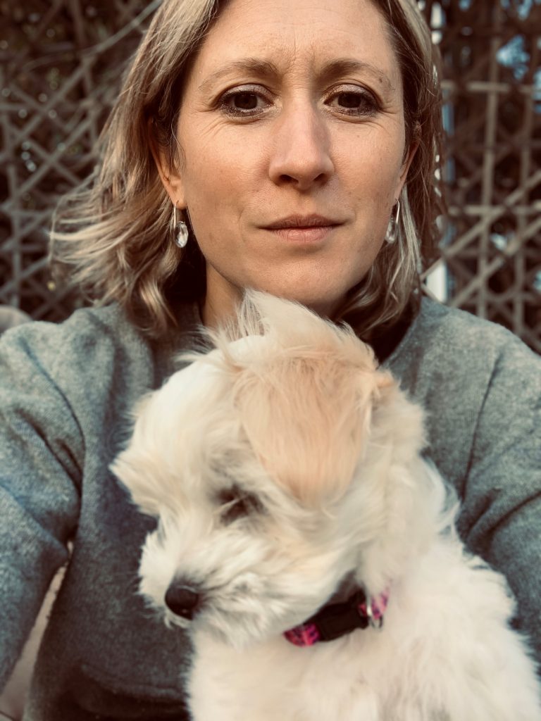 Emma Gray is looking at the camera with a small white dog.