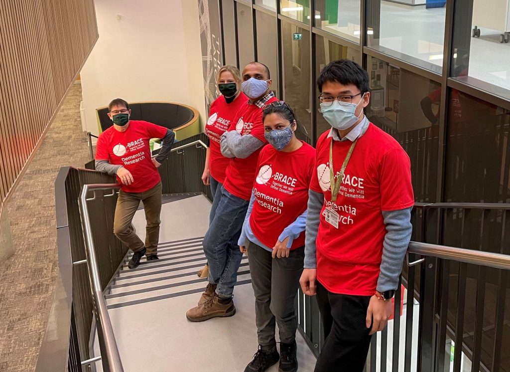 Exeter University team of 4 people standing on stairs in red BRACE t-shirts and wearing face masks