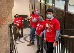 Exeter University team of 4 people standing on stairs in red BRACE t-shirts and wearing face masks