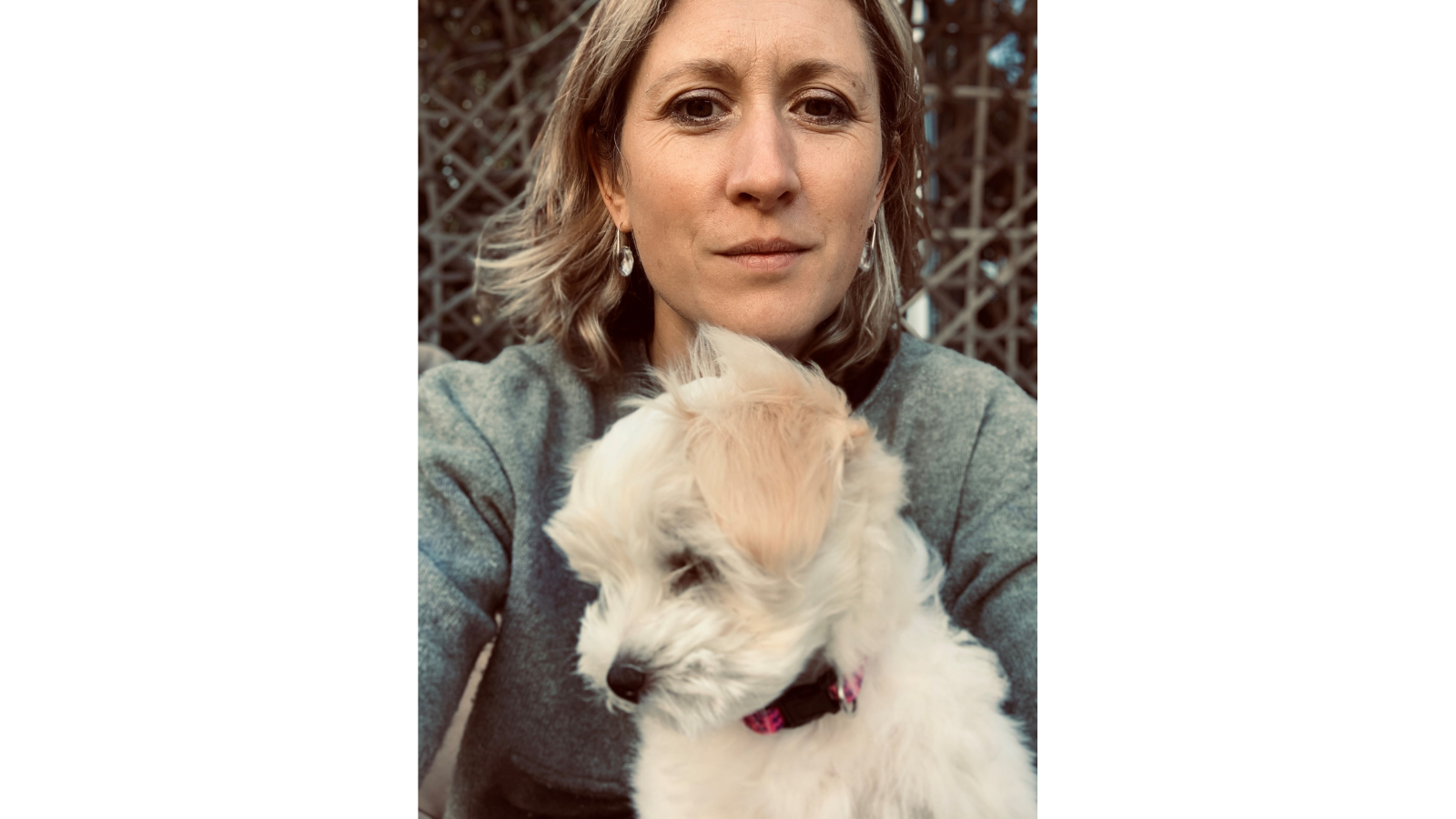 Emma Gray is looking at the camera with a small white dog.