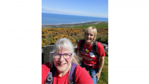 Eirlys and Linda are walking with BRACE t-shirts on, there is hills and the sea in the background