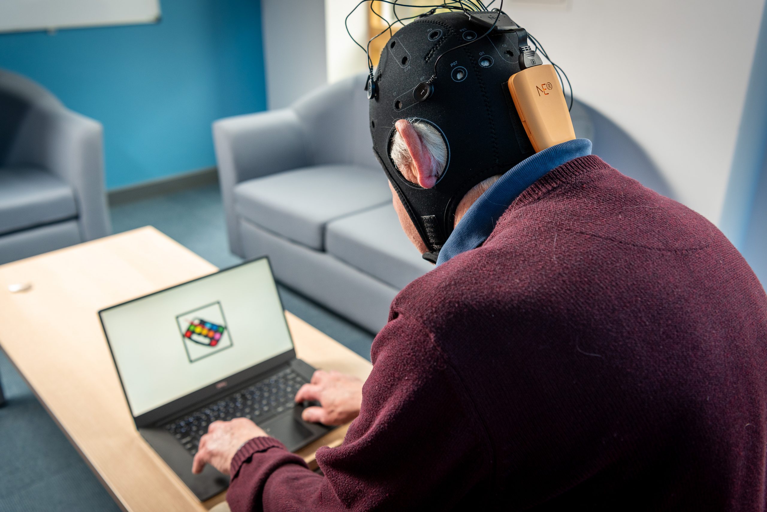 Man with EEG cap on watching a laptop with flashing images.