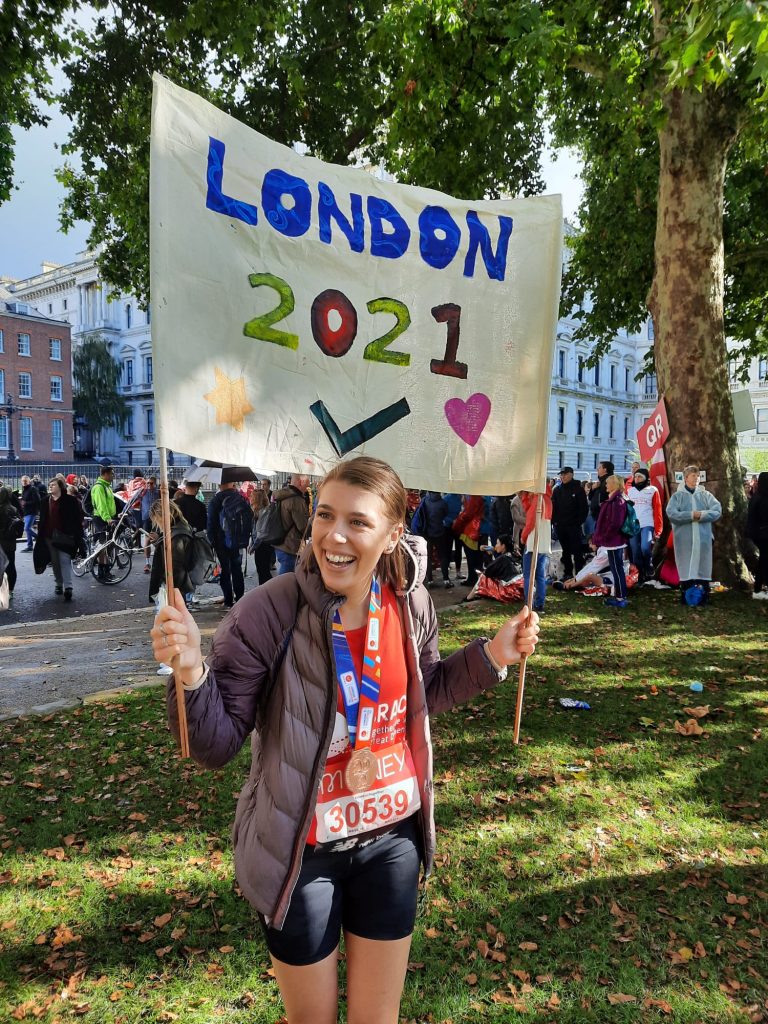 Rhiannon is stood with a banner saying London 2021