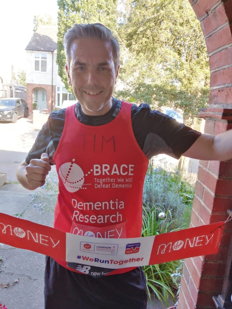 Tim is stood in his BRACE top pretending to finish the marathon at his home.