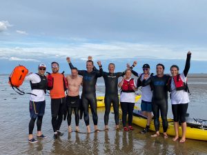 10 swimmers stood on the beach in wetsuits by the sea