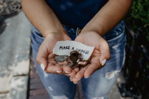 Hands cupped together with coins and the words ' make a change' on a piece of paper.