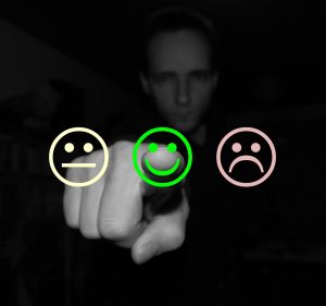 Man pointing his index finger toward a smiley emoji in the middle. On either side of the smiley emoji is an ok face and a sad face.