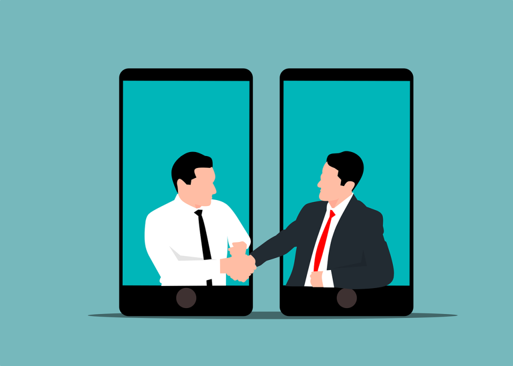 Illustration of two mobile phones next to each other. There are two suited men with ties reaching from the phones to each other to shake hands. The background is a green colour.