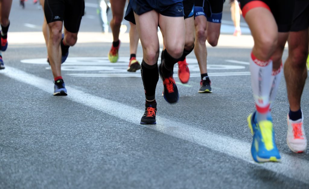 Lots of runners legs running on a concrete pavement.