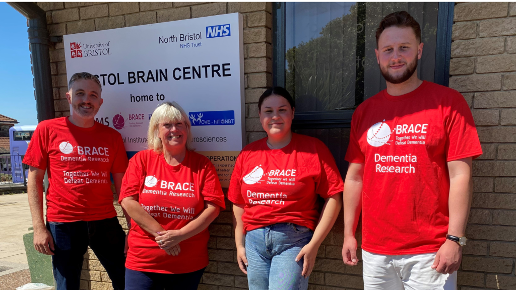 Four people are stood outside the Bristol Brain Centre. The are all wearing BRACE red t-shirts.