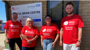 Four people are stood outside the Bristol Brain Centre. The are all wearing BRACE red t-shirts.
