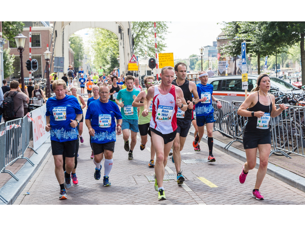 A large group of runners have just runner over a bridge as part of the Amsterdam Marathon race course.