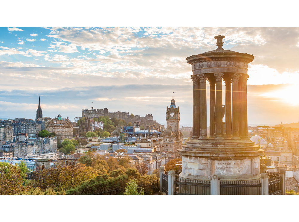 A landscape photo of Edinburgh on a sunny day. Lots of landmarks including Edinburgh castle are in the photo.