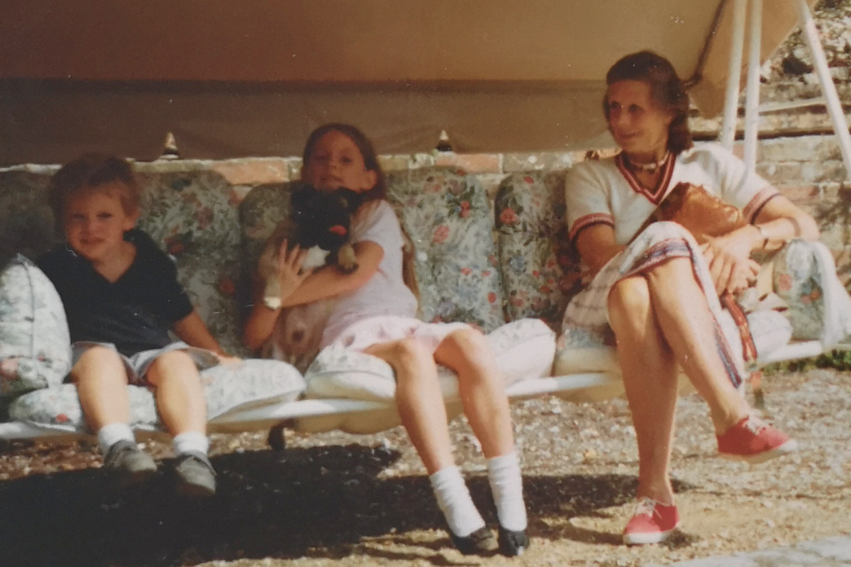 Laura and her brother as children, sat on a swing chair with their granny.