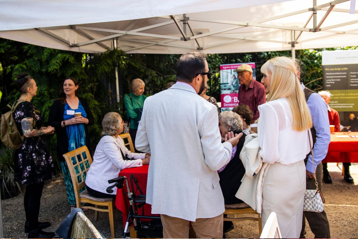 Separate groups of people, standing and sitting, are having conversations underneath a marquee.