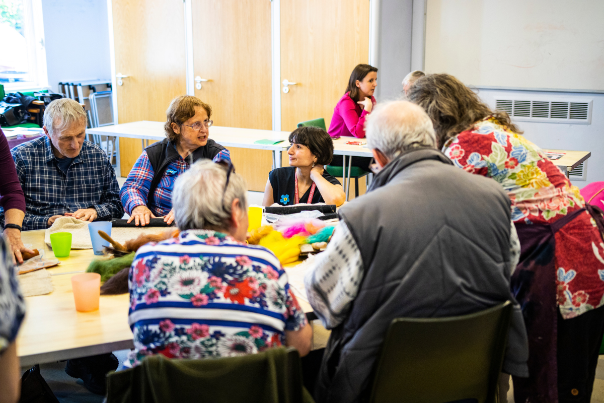 A group of people make felt art while sat around a table.