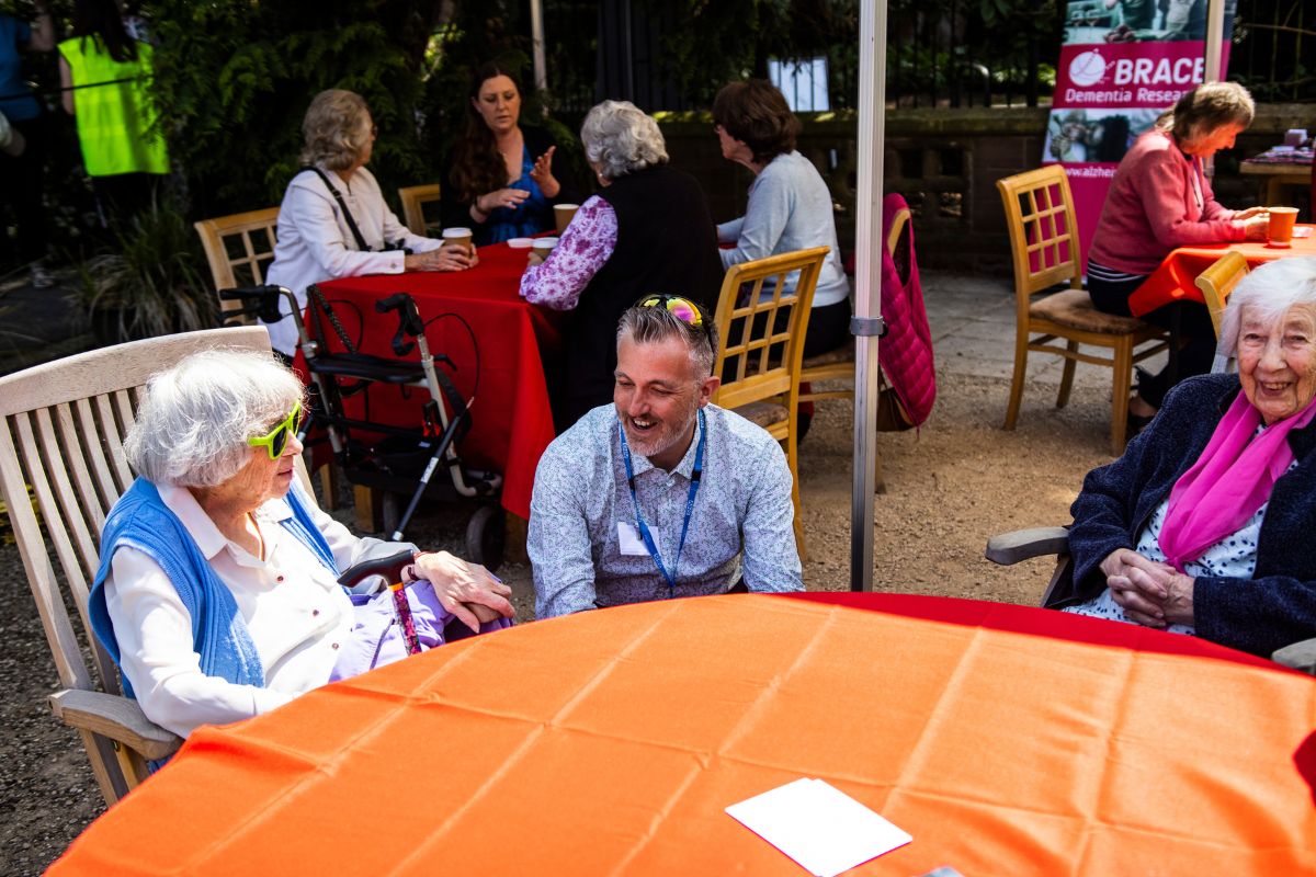 A group of people talk and laugh while sat around a table.