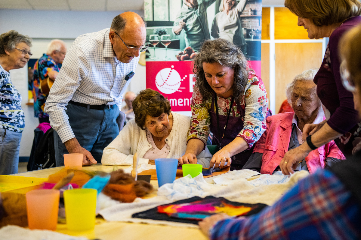 A woman teaches a group of people how make felt art while sat around a table.