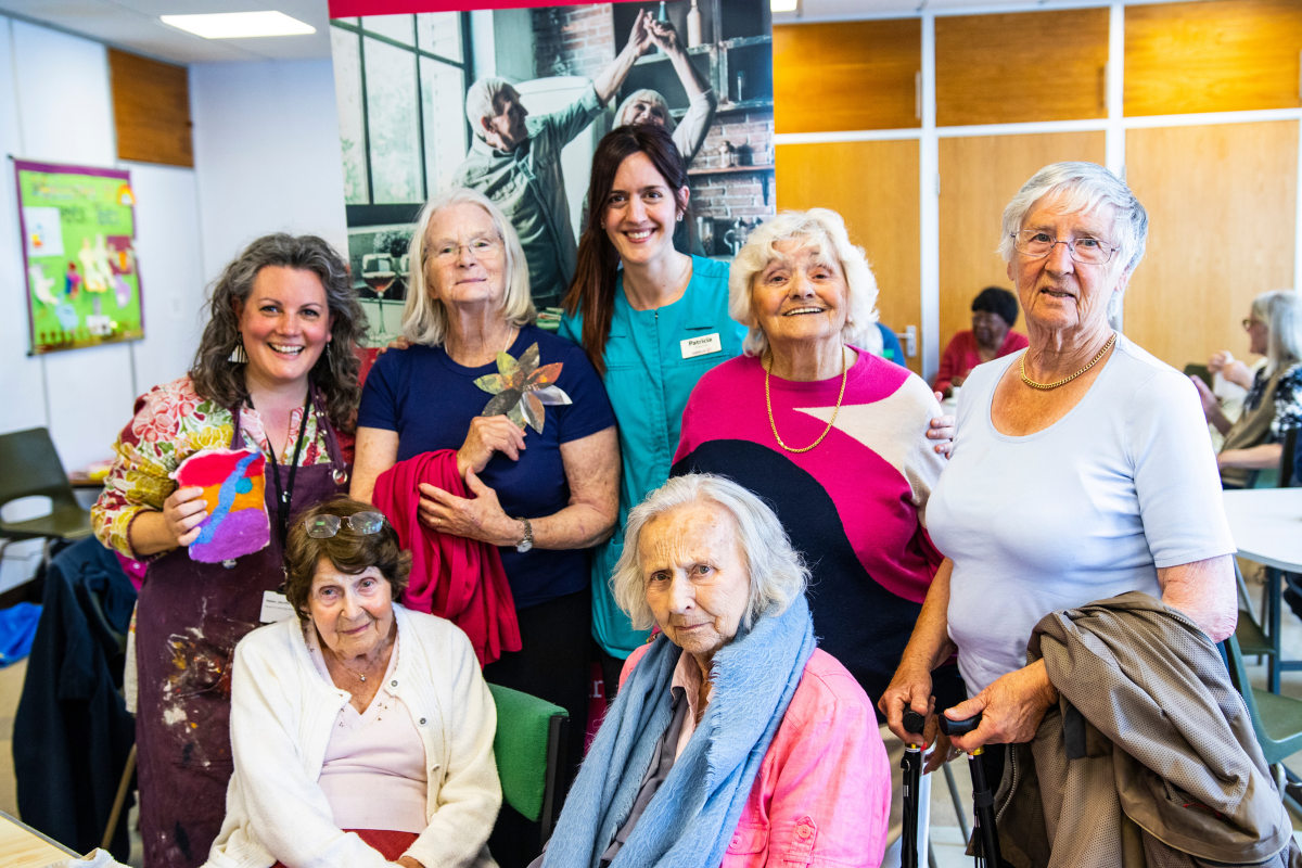 A group of seven people, including a carer, smile for a photo as they look at the camera.