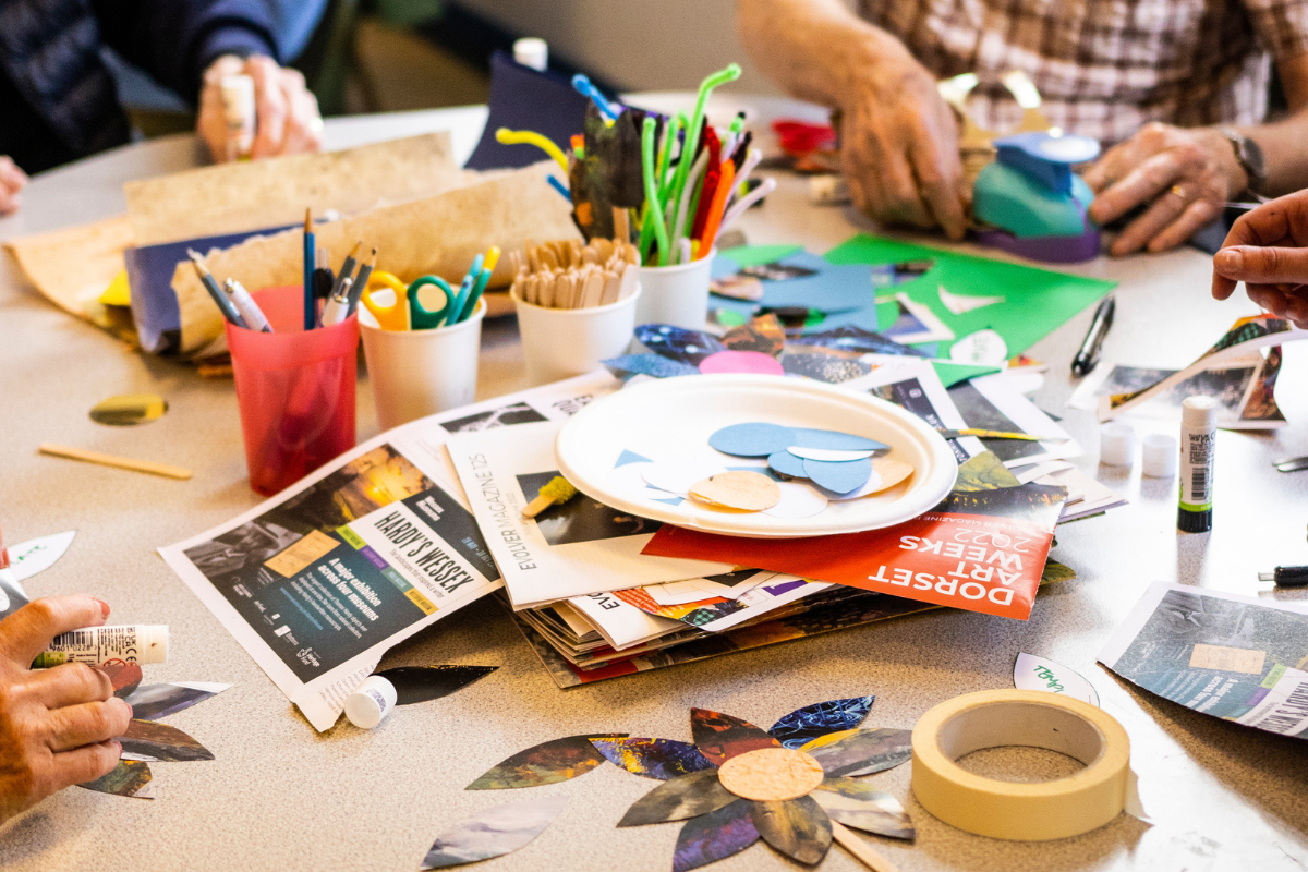 A variety of materials and tools on a table as people use them to make art.