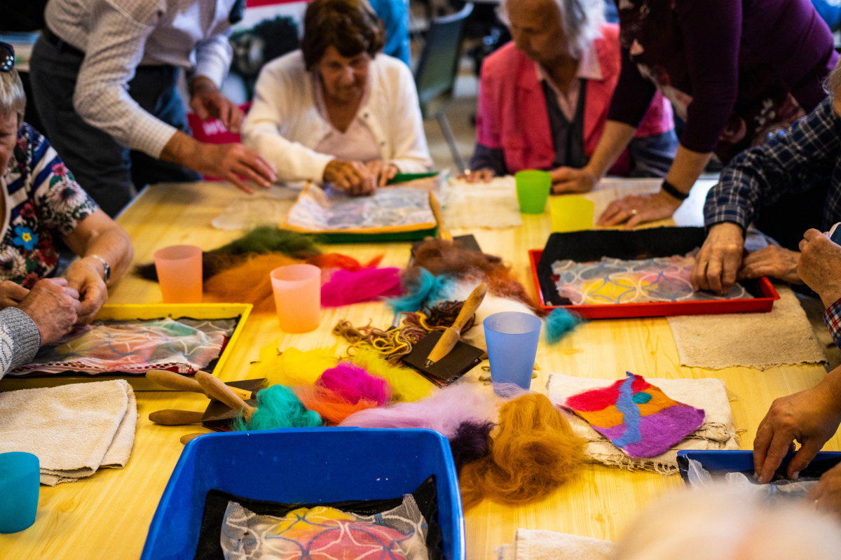 A group of people are sat around a table learning how to make felt art.