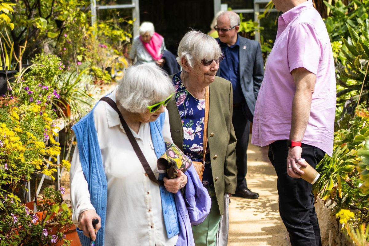 A group of people observe a variety of plants and cacti inside a greenhouse.