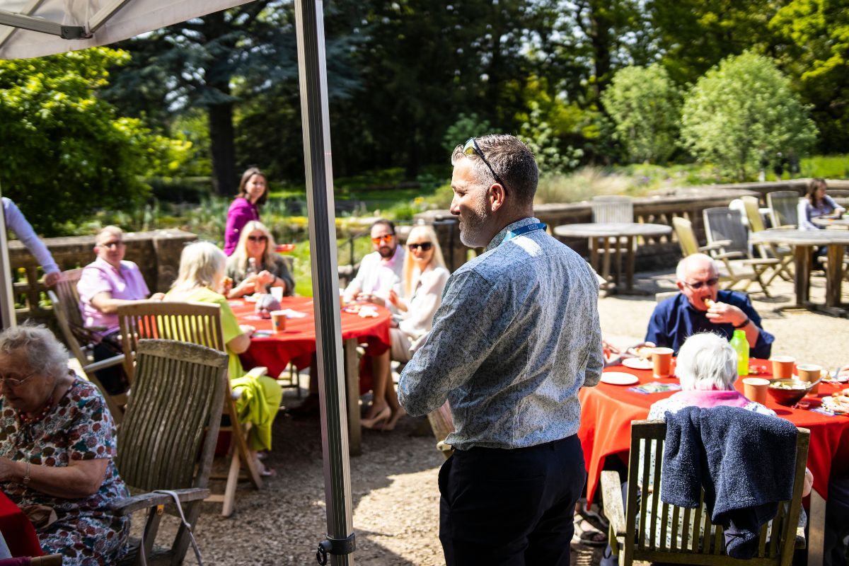 BRACE Director makes a speech to a group of people who are sat down having afternoon tea.