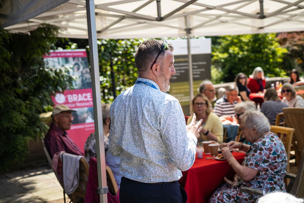 BRACE Director makes a speech to a group of people who are sat down having afternoon tea.