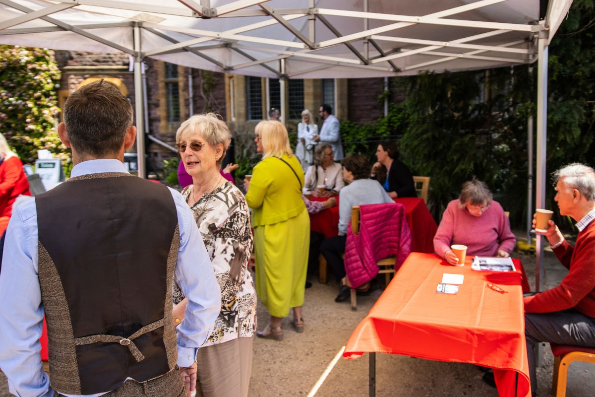 Groups of people converse between each other as they have afternoon tea underneath a marquee.