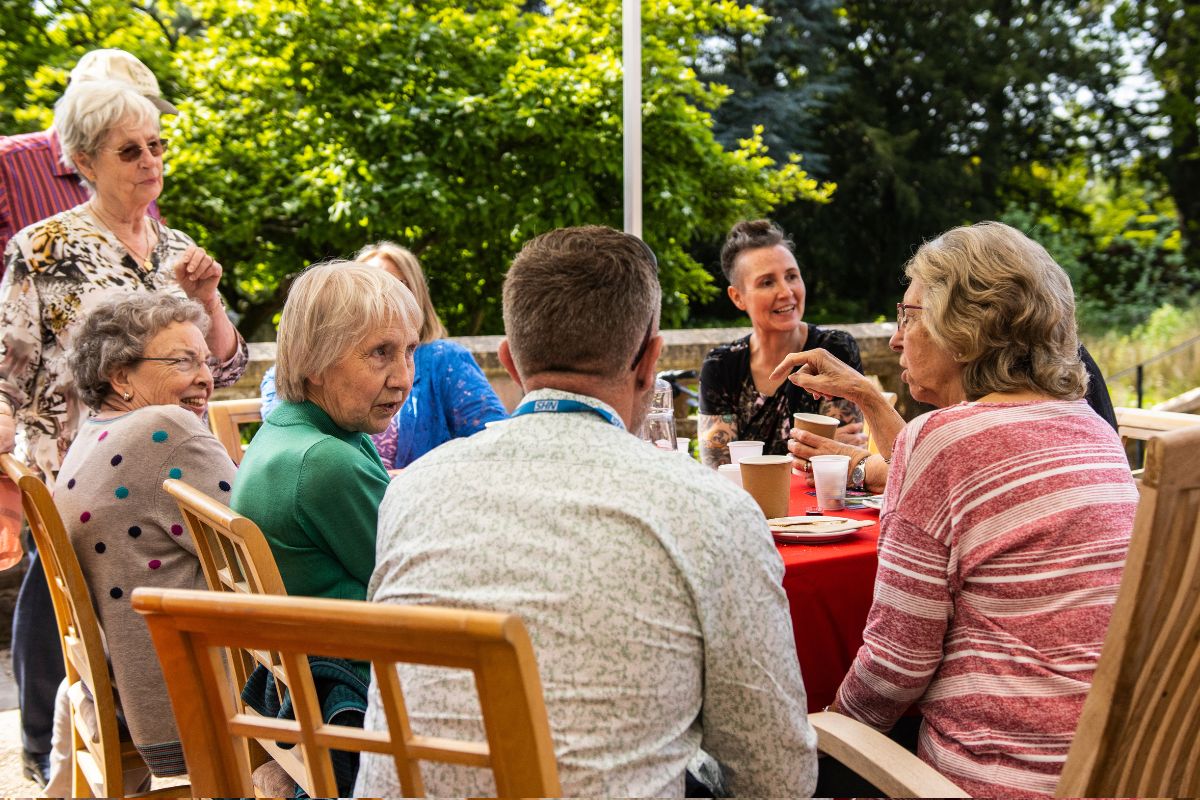 A group of people have a conversation sat around a table with lunch.