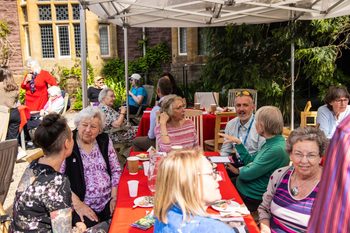 Groups of people converse between each other as they have afternoon tea underneath a marquee.