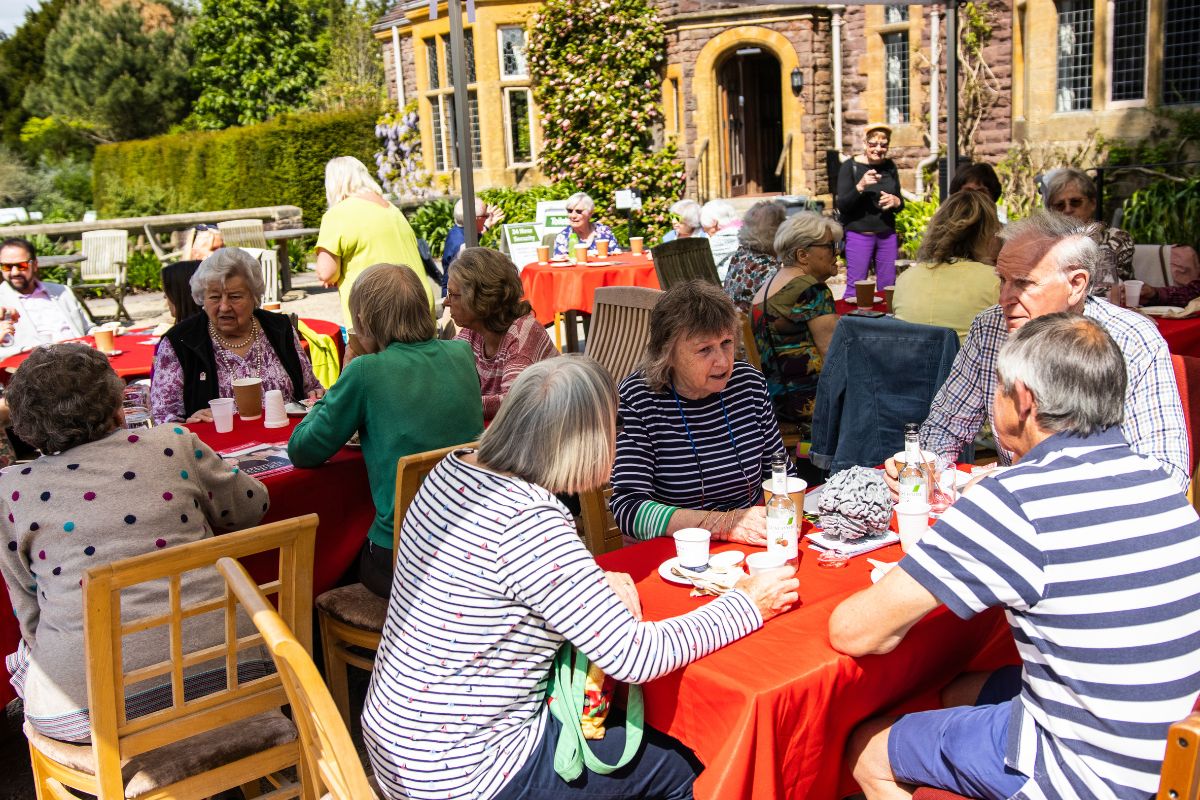 Groups of people converse between each other as they have afternoon tea underneath a marquee.