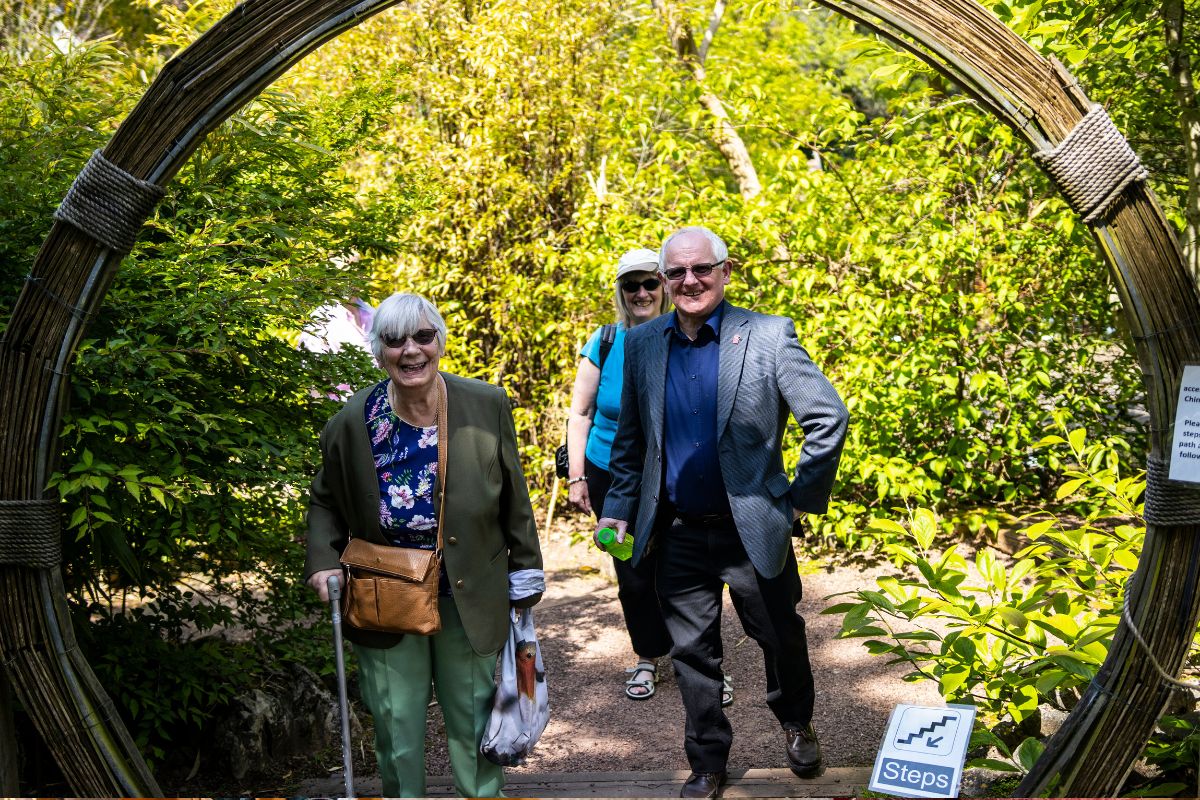 A man and two women smile as they walk through an archway surrounded by greenery.