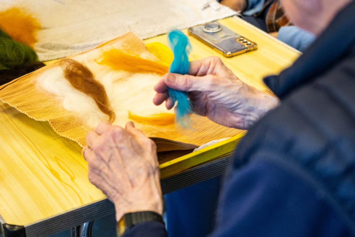 A man is sat at a table making felt art with his hands.