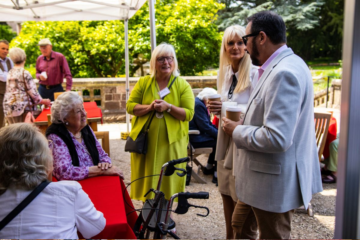 A group of people, standing and sitting, are having conversations underneath a marquee.