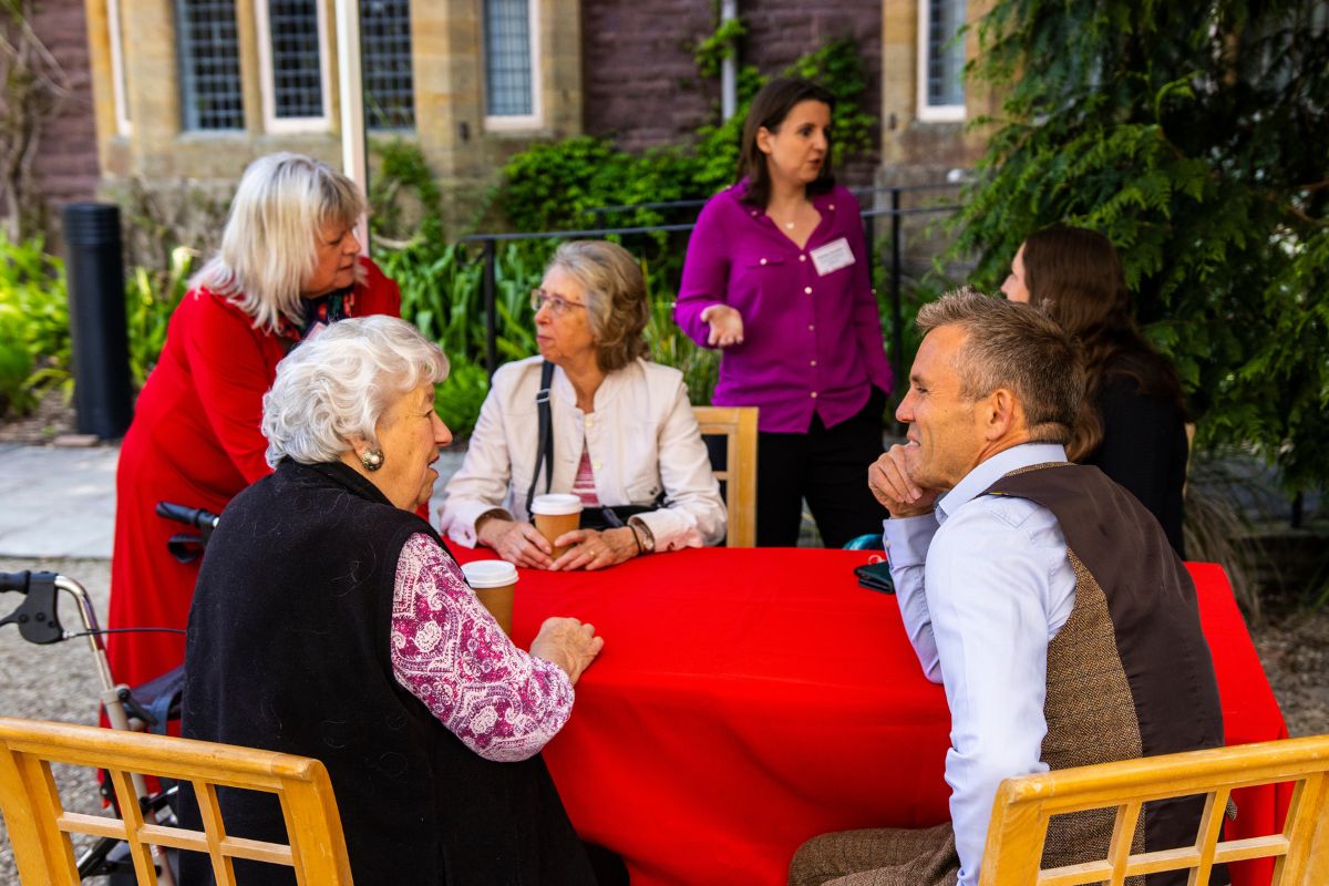 A group of people have a conversation sat around a table with tea and coffee.