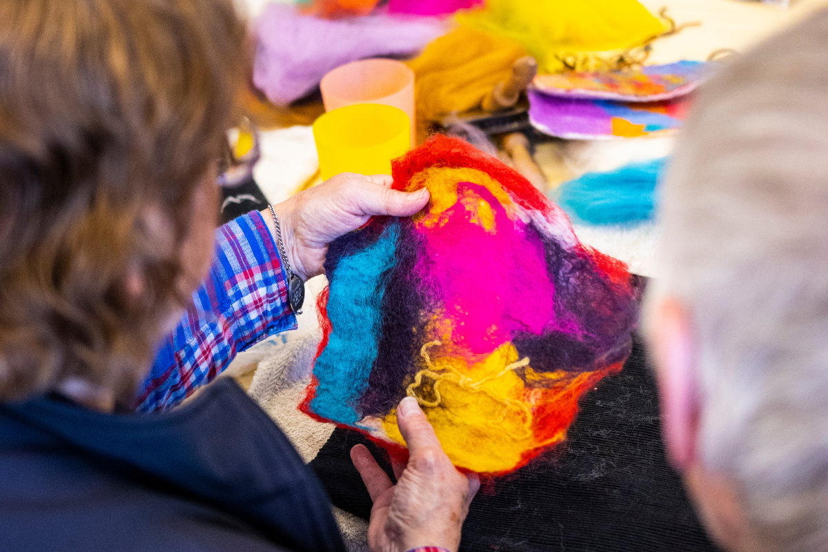 A man and a woman sat at a table look at their finished multicoloured felt art.