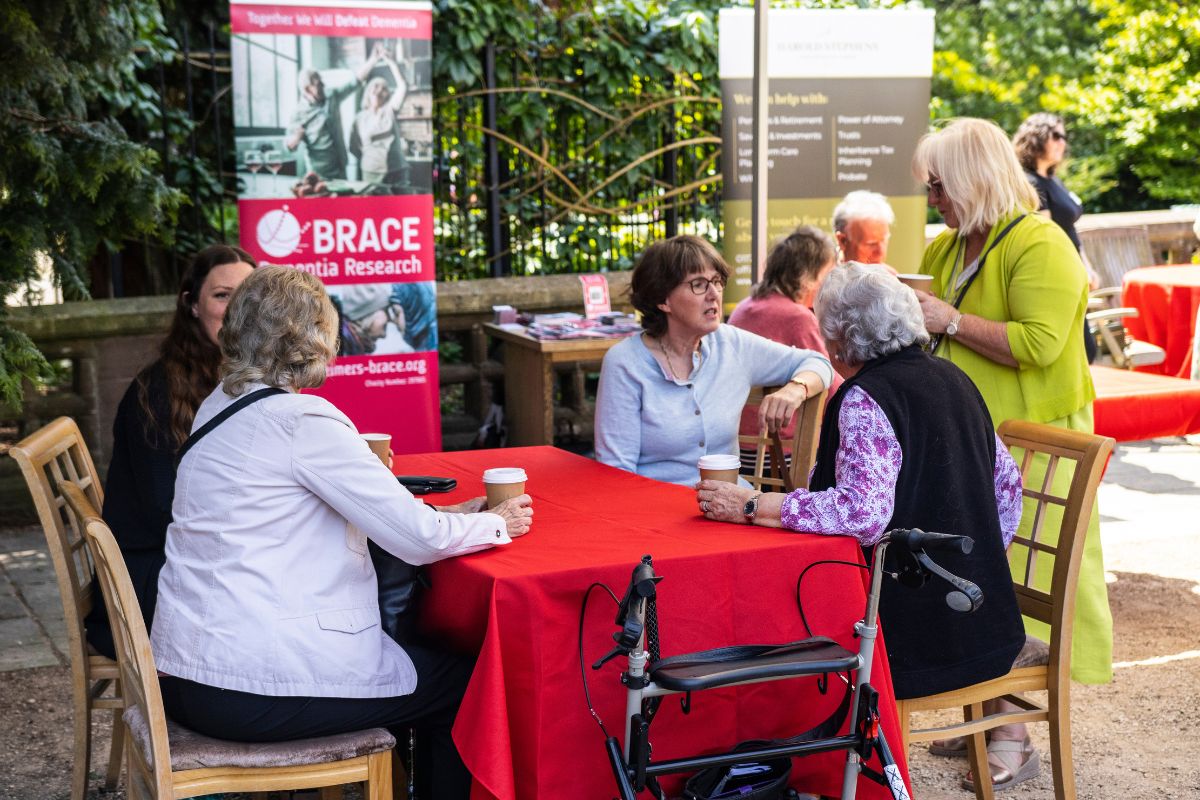 A group of people, standing and sitting, are having conversations underneath a marquee.