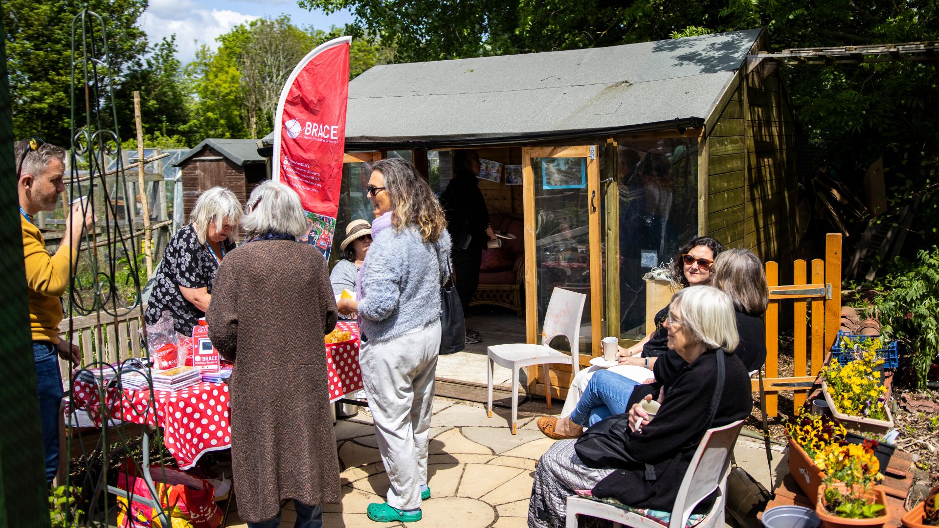 A group of people sitting and standing converse at the Alive Allotments.