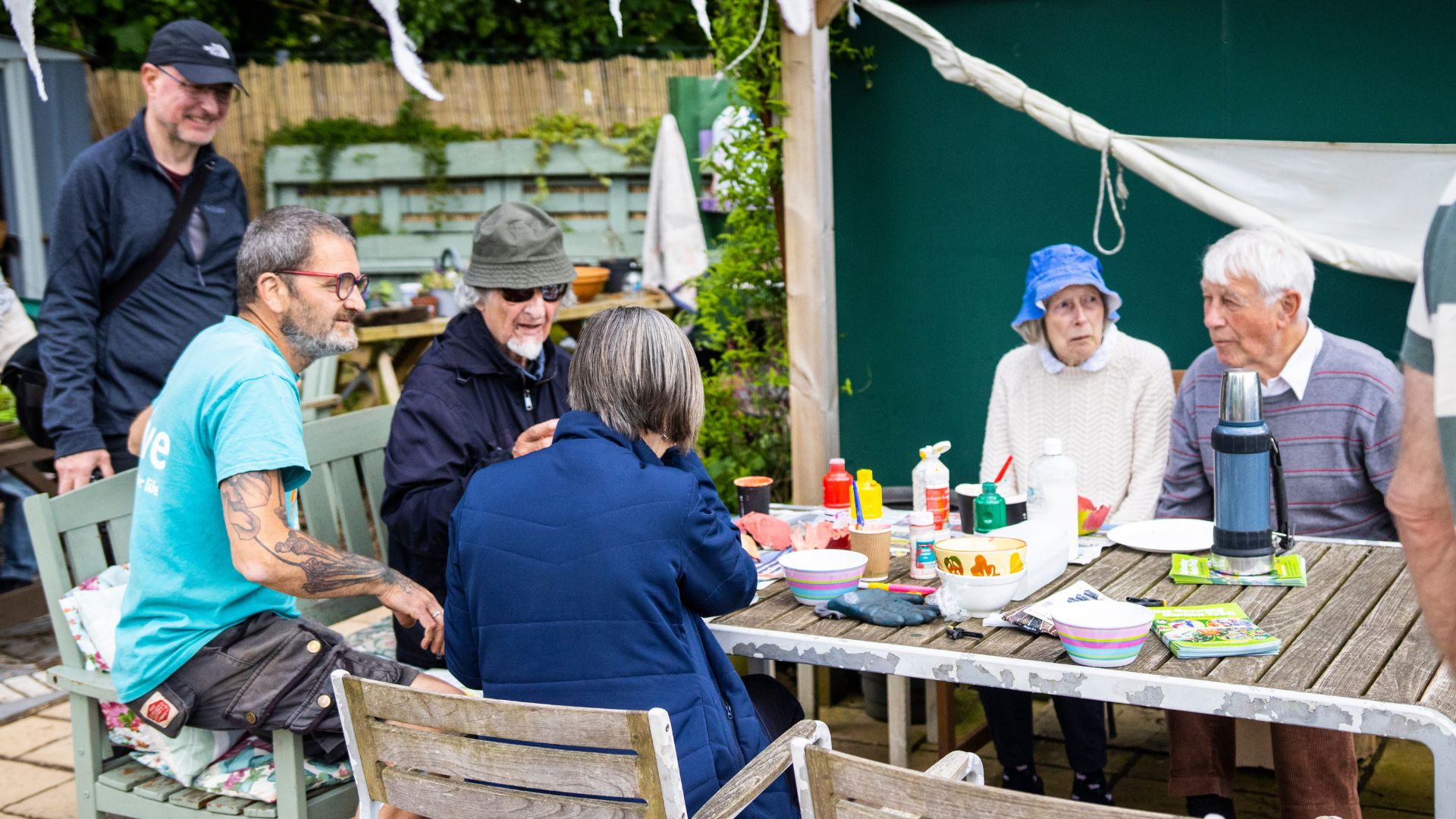 A group of people sat around a table create art and converse between each other.