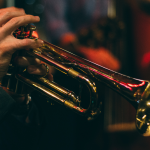 A trumpet is being played, only the hands of the player can be seen.