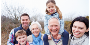 Grandparents, with their adult children and grandchildren outside, smiling.