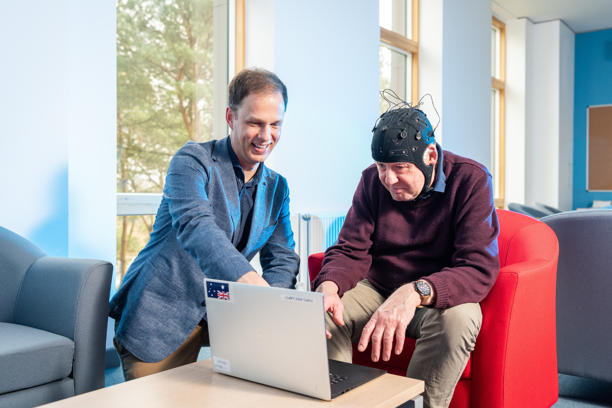 Researcher George Stothart and a man wearing a cap with wires doing tests on a laptop.