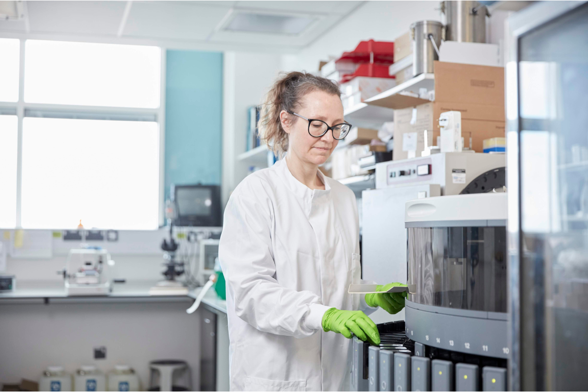 A woman wearing a lab coat and green gloves in the South West Dementia Brain Bank.