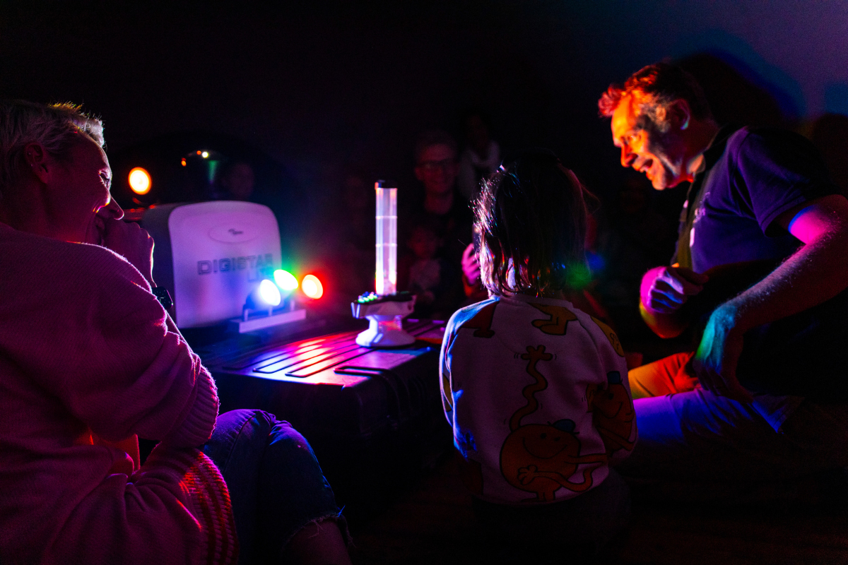 A child and two adults are sat in the dark testing a brain wave game.