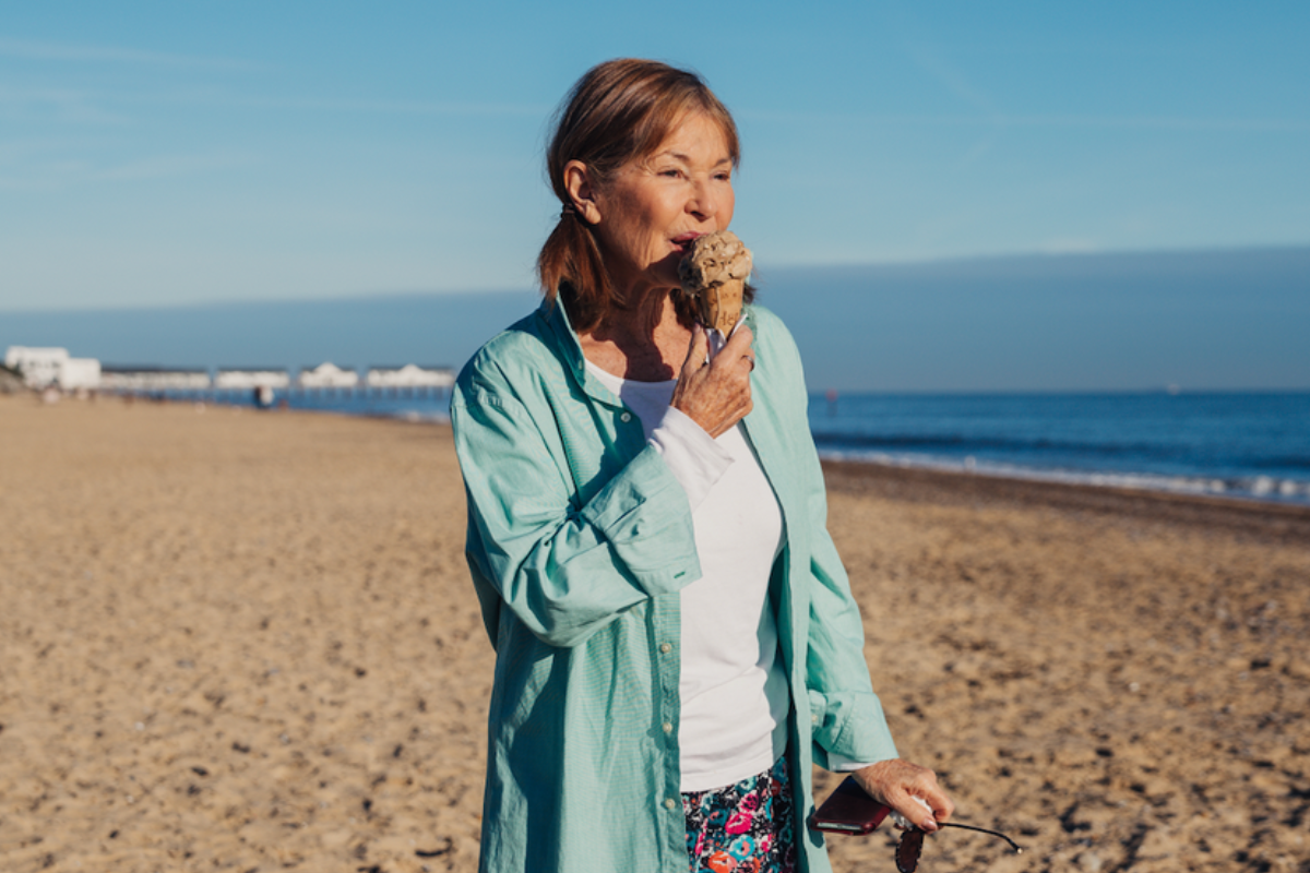 Stephanie Beacham eating an ice cream while standing on a beach.