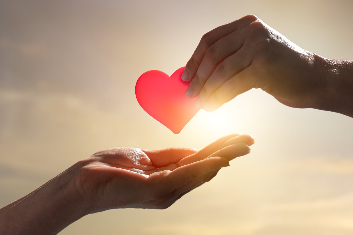Two hands, with one passing a red heart to the other.